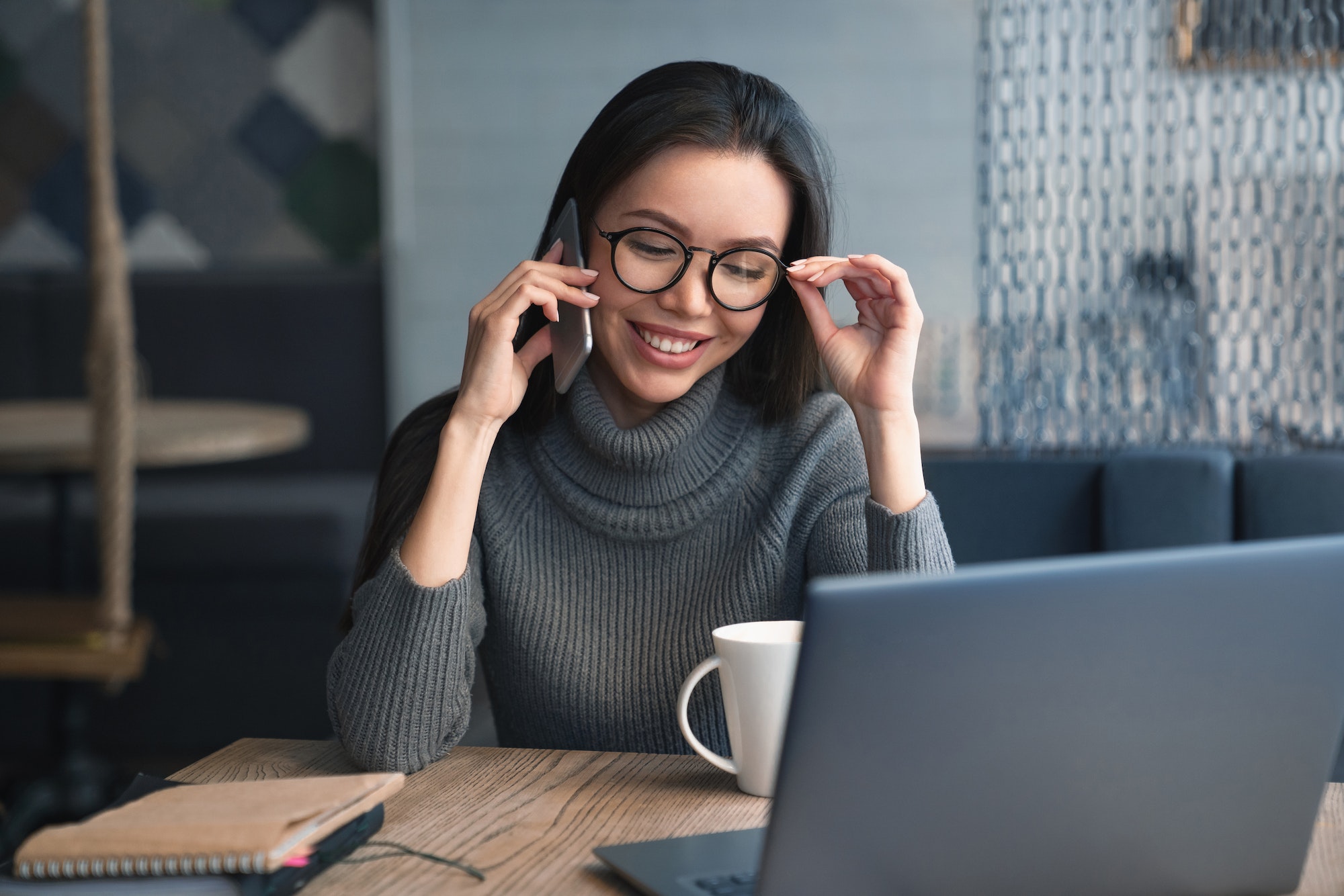 Cheerful female executive have conversation by mobile phone with client at coworking place